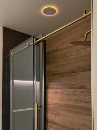 Upper glass rail and showerhead beside wood-tone shower tile