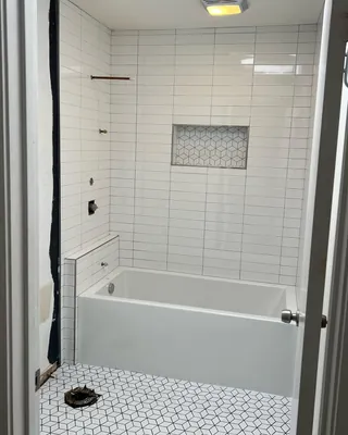 White rectangular tub-surround tile with a geometric mosaic niche and floor