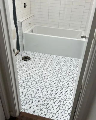 Geometric mosaic floor beside a white bathtub and tiled tub-end ledge