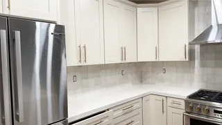 Glossy pale square tiles wrap a kitchen counter corner beside white cabinetry and stainless appliances.