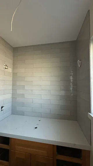Pale gray glossy rectangular tiles wrap a counter alcove above a white top and wood-tone cabinet.