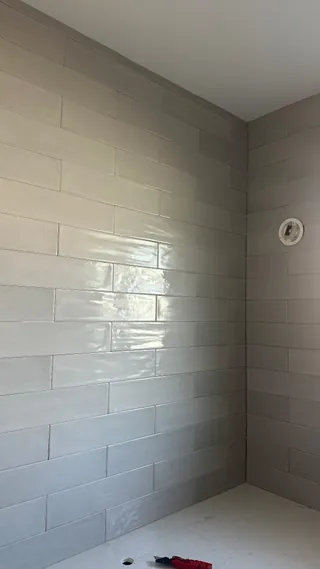 Glossy pale gray rectangular wall tiles form offset rows around the right corner of a counter alcove.