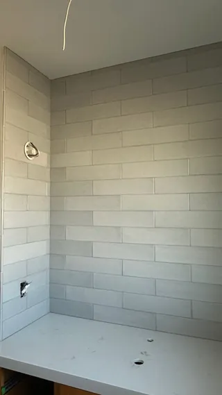 Pale gray running-bond rectangular tile meets a white countertop in an inside corner.