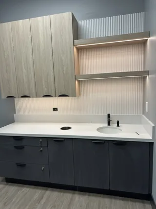 Pale ribbed backsplash behind a round sink with wood-tone shelves and cabinets