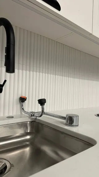 Metal sink and tap in front of a pale vertically ribbed backsplash