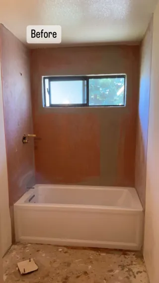 White bathtub below a horizontal window with exposed surrounding wall surfaces before tiling.