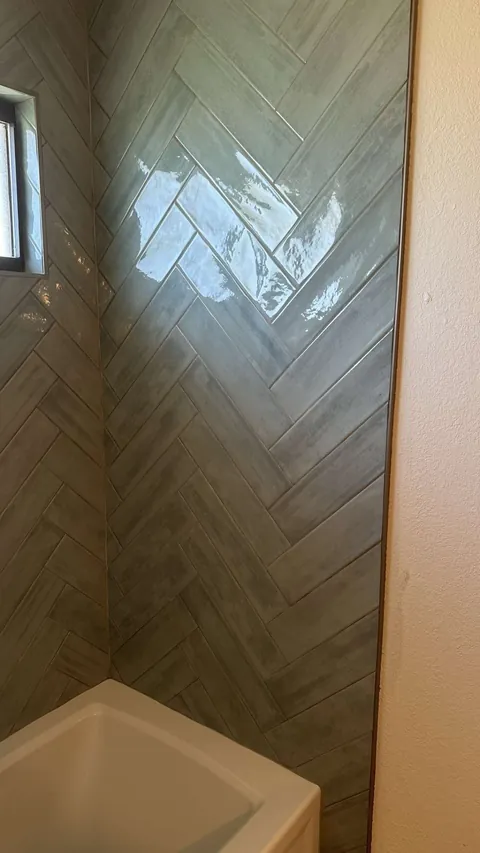 Glossy blue-gray herringbone tile meeting at the right corner above a white bathtub, with edge trim beside the painted wall.