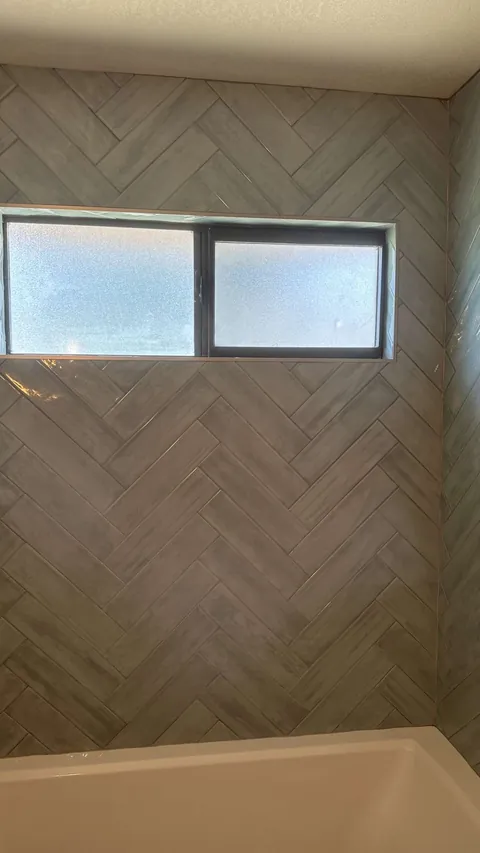 Blue-gray herringbone tile around a horizontal frosted window above a white bathtub.
