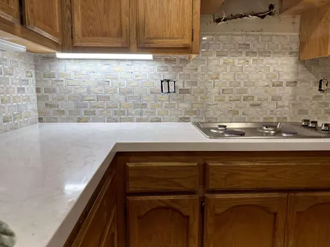Interlocking rectangular mosaic backsplash beneath wood cabinets and around a cooktop, with uncovered outlets.