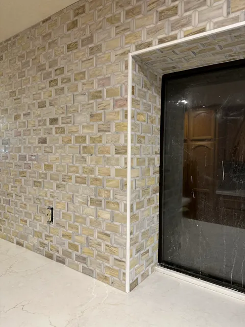 Close view of cream and gray rectangular mosaic pieces and pale edge trim beside a dark kitchen window frame.