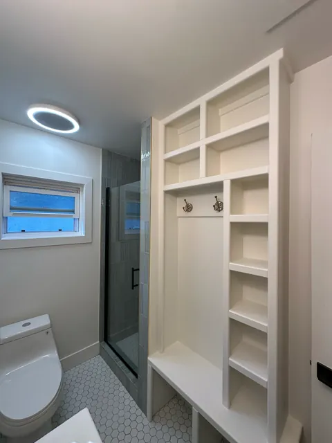 White open shelving beside a glass shower, hexagonal tile floor and window.