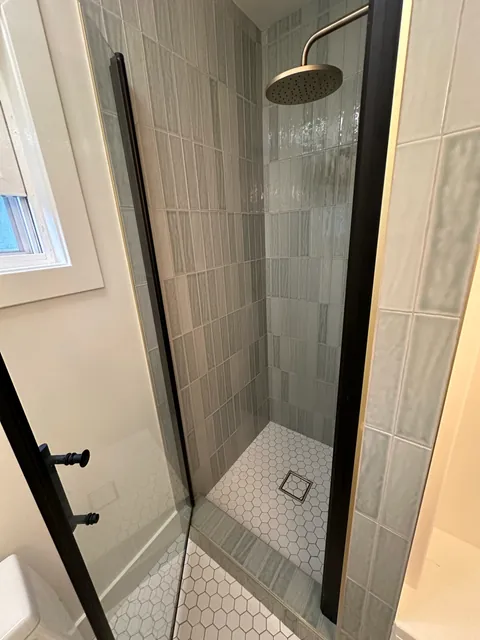 Vertical gray-green shower wall tile, warm-metal shower head and white hexagonal shower floor.