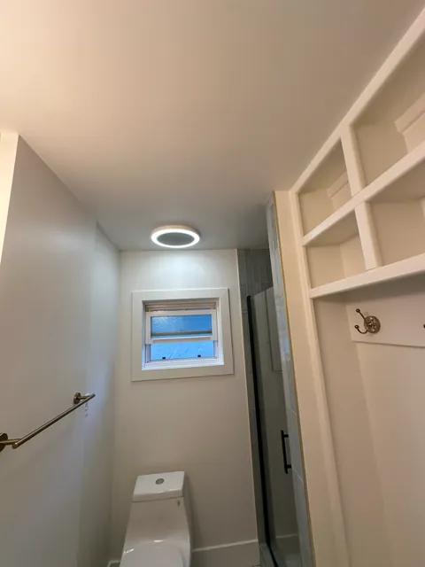 Bathroom window, circular ceiling light and open shelving beside the glass shower.