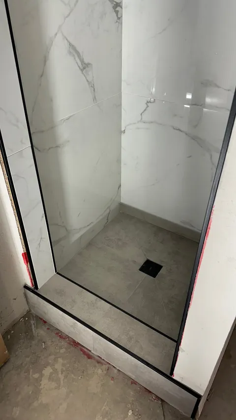 Gray shower floor tiles meet a square black drain beneath white veined wall tile.