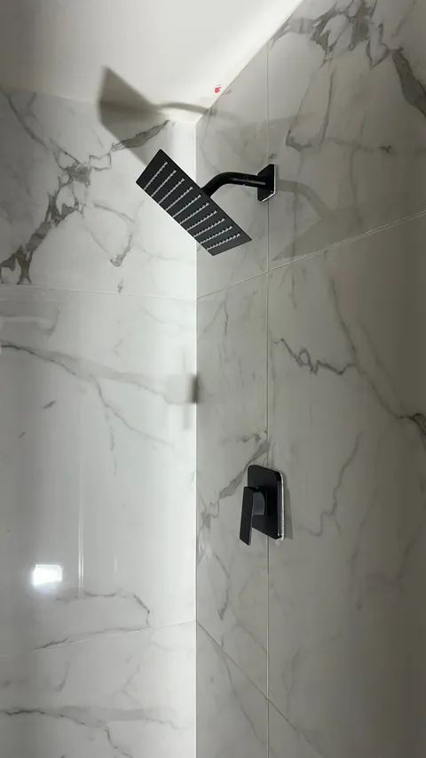 Square black shower head and black control against white wall tile with gray veining.