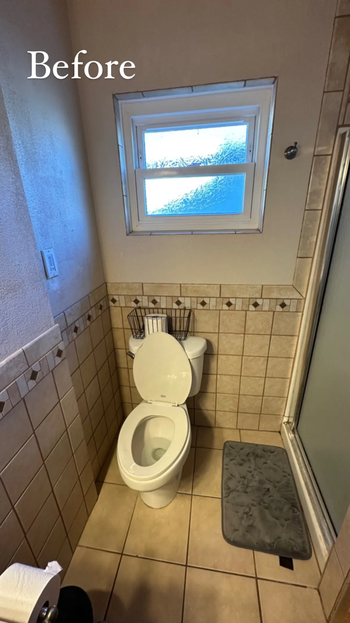 Narrow bathroom with beige square wall and floor tile, a decorative border and a toilet beneath the window.
