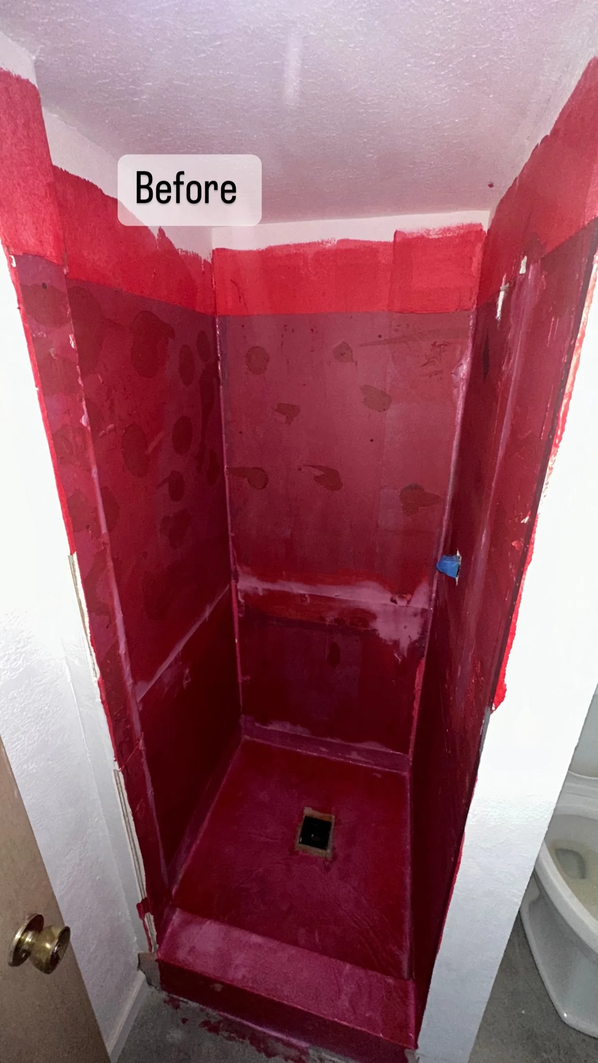 Compact shower at a red-coated preparation stage, with a square drain opening and raised threshold.